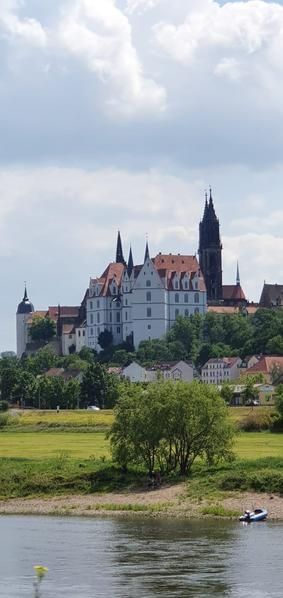 Historisches Schloss mit roten Dächern und hohen Türmen mit Blick auf eine grüne Landschaft und einen Fluss