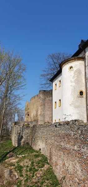 Eine historische Burgmauer und ein weißes Gebäude mit gelben Fenstern